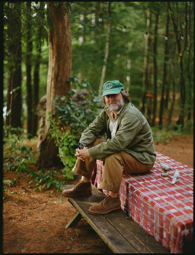Man sitting on a bench in a forest with a green cap and plaid blanket